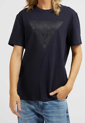 Personne portant un t-shirt noir à manches courtes avec un motif en triangle noir texturé pointant vers le bas, associé à un jean bleu.