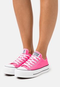 Baskets en toile rose avec des lacets blancs et des semelles en caoutchouc. Présentent une bande noire le long de la semelle et une étiquette sur la languette.