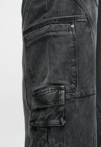 Krupni plan crnih traperica s bočnim džepovima i detaljnim prošivanjem na tkanini.