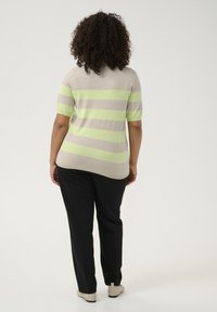 Pulover ușor, bej, din tricot, cu dungi verzi și gri. Are mâneci scurte și un tiv curbat. Asortat cu pantaloni negri.