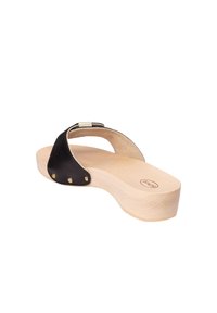 Svart lädersandal med träplattform, med en metallisk detalj nära remmen och mässingsnitar på sidan.