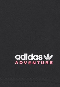 Tessuto nero con superficie liscia caratterizzato dal logo bianco "adidas" e dal testo rosa "ADVENTURE". Design semplice senza ulteriori motivi o elementi decorativi.