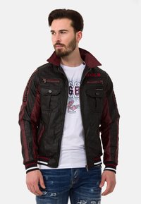 Schwarze und burgunderrote Jacke mit strukturierter Oberfläche, ausgestattet mit Reißverschlusstaschen, einem hohen Kragen und gestreiften Rippbündchen.