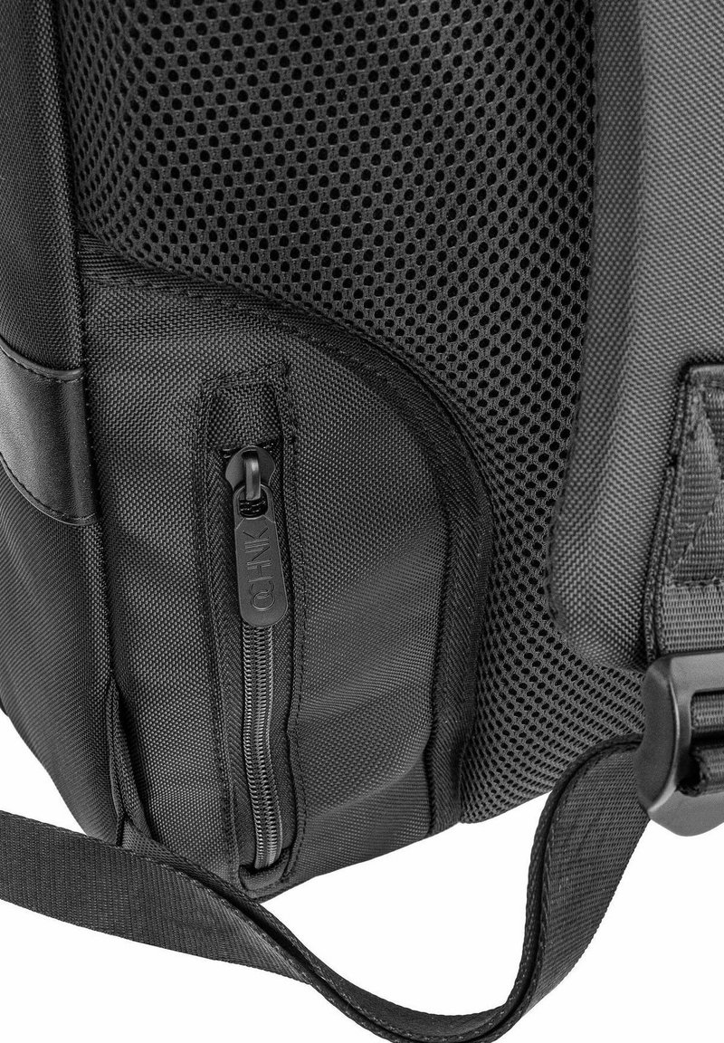 Bolso de tela de malla negra y texturizada con un bolsillo lateral con cremallera, correa ajustable y accesorios de plástico. Presenta un diseño elegante y funcional.