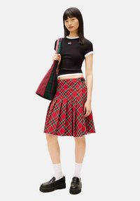 Černý krátký top s bílým lemováním, doplněný červenou károvanou plisovanou sukní. Černé platformové boty a kabelka se stejným károvaným vzorem dokončují vzhled.