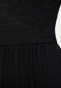 Μαύρο φόρεμα με δαντέλα σε σχέδιο λουλουδιών στο πάνω μέρος του κορσέ και λείο, πιετάριστο ύφασμα στη φούστα.