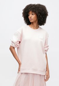 Ροζ φούτερ με στρογγυλή λαιμόκοψη, μακριά μανίκια και άνετη εφαρμογή. Διαθέτει υφασμάτινη λεπτομέρεια με λογότυπο στο στήθος και τρεις λευκές ρίγες στα μανίκια.