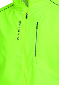 Lys neon gul jakke med lynlås foran, der har reflekterende detaljer og et "ELITE LAB" logo. Fremstillet af glat, let materiale.