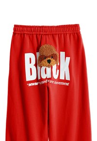 Los pantalones deportivos rojos presentan un gran estampado blanco que dice "Negro" y una aplicación de un perro marrón de peluche en la parte frontal. Cintura elástica para mayor comodidad.