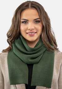 Fular de culoare verde închis, realizat dintr-un material moale, cu margine ribelată și stil drapat, purtat peste un palton bej deschis.