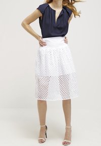 Tmavě modrá halenka s krátkými rukávy a průstřihem na krku doplněná bílou texturovanou sukní ke kolenům s perforovaným vzorem a elastickým pasem.