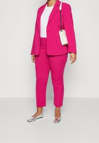 Fuchsia skräddarsydd blazer och matchande slim-fit byxor, parat med en vit topp och silvriga flats. Outfiten har rena linjer och en strukturerad design.