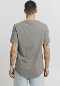 Gray, short-sleeve T-shirt with a round neckline and a curved hem. Made of soft cotton fabric. Features visible tattoos on arms.
