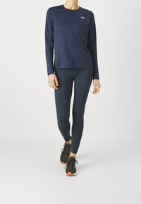 Granatowa bluzka z długim rękawem i zaokrąglonym dekoltem, w zestawie z granatowymi legginsami. Do tego czarne buty sportowe z pomarańczowymi akcentami.