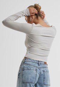 Lys grå langermet topp med en tettsittende design og en subtil glans, kombinert med blå denim høyt liv jeans med baklommer.