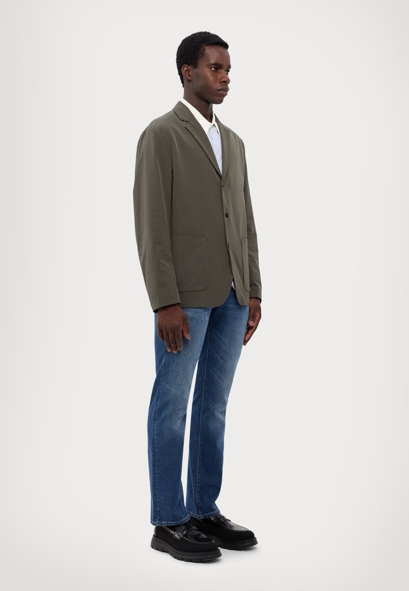 Olive green blazer with a single button, two front pockets, white collared shirt with blue stripes, blue denim jeans, and black platform shoes.