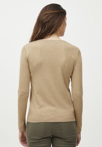 Beige ilgos rankovės megztinis su apvalia iškirpte ir raštuotais kraštais. Minkštas mezgimo audinys su paprastu, prigludusiu dizainu. Nėra matomų raštų ar akcentų.