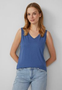 Blaues ärmelloses Top mit V-Ausschnitt, aus glattem Stoff gefertigt. Es hat eine lockere Passform und wird mit hellblauen Jeans kombiniert.