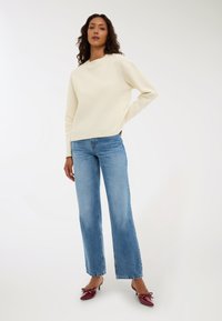 Kremowy, lekki sweter z dzianiny o okrągłym dekolcie, w połączeniu z jasnoniebieskimi spodniami z szerokimi nogawkami i bordowymi klapkami na obcasie.