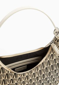 Beżowa torba na ramię z fakturowanego materiału z czarnym geometrycznym wzorem. Wnętrze zawiera czarne podszewkę oraz kieszeń na zamek.