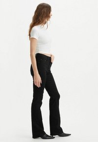 Zwarte uitlopende jeans met een hoge taille, voorzien van een zachte textuur en een vijfzakken ontwerp, gecombineerd met een fitted wit T-shirt en zwarte schoenen.