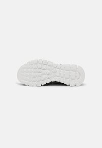 Semelle d'une basket noire montrant une semelle extérieure en caoutchouc blanc texturé avec un motif de grip carré et rectangulaire pour la traction.