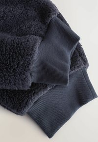 Marineblå fleece og ribstrikket stof lagd ovenpå hinanden, der fremviser blød, tekstureret fleece og kontrastfyldte glatte ribkanter.