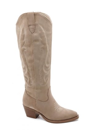 Botte en daim beige, hauteur cheville, avec un bout pointu, un design contour et une couture décorative blanche. Talon légèrement rehaussé et languette.