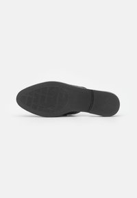 Semelle de botte en cuir noir avec motif de bande de roulement texturé sur fond gris clair, vue du dessous.