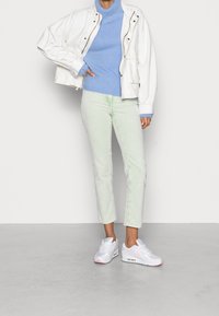 Vit kort jacka, ljusblå ribbad polotröja, pastellgröna raka jeans och vita sneakers med rosa detaljer.