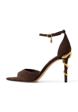 Sandale à talon haut en daim marron avec bride à la cheville et détail serpent doré s'enroulant autour du talon sur fond blanc.