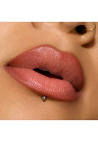 Colore labbra rosa tenue con texture liscia, caratterizzato da un piercing labiale argentato. Le labbra sono piene e leggermente aperte, rivelando un contrasto di colore interno.