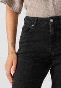 Svarta högmidjade jeans i denim, med knäppning fram, femficksdesign och en texturerad yta.