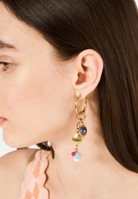 Guldörhänge med en blå pärla, snäcka charm, och flerfärgade pärlor i rosa, turkos och vitt, hängande från en kedja.