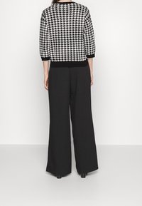 Pull noir et blanc à motif pied-de-poule avec manches retroussées, assorti à un pantalon noir à jambes larges, affichant une silhouette décontractée.