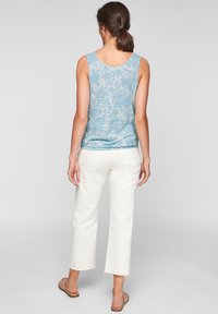 Niebieski top na ramiączkach w kwiatowy wzór z zaokrąglonym dekoltem, zestawiony z kremowymi, krótkimi spodniami i beżowymi sandałami. Gładka tkanina i luźny krój.