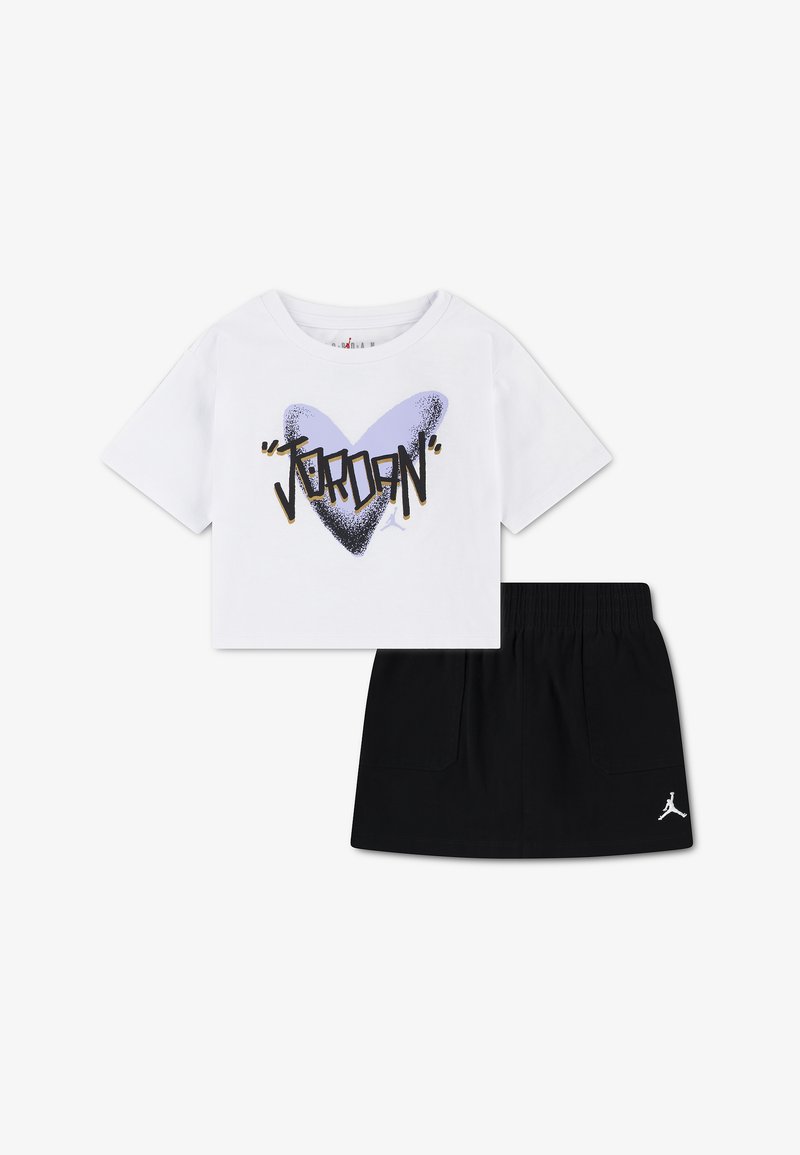 Crop top blanc à manches courtes avec un cœur violet et le texte « Jordan », associé à une jupe noire à taille élastique ornée d'un petit logo Jumpman blanc.