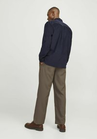 Camicia blu navy con maniche lunghe, colletto a contrasto e vestibilità comoda, abbinata a pantaloni larghi marroni e scarpe marroni scure.