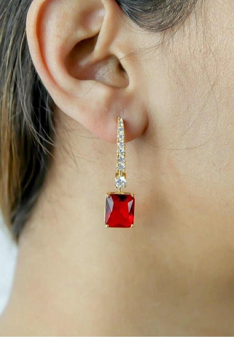 Boucle d'oreille en or avec une pierre précieuse carrée rouge et de petites pierres claires portée à l'oreille gauche d'une femme à la peau claire et aux cheveux foncés.