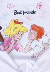 T-shirt bianco con una grafica a fumetti di due ragazze, una con i capelli gialli e un fiocco rosso, l'altra con i capelli rosso-bruni, entrambe sorridenti.