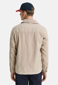Beige Baumwolljacke mit einem Kragen im Hemdenstil, Knopfmanschetten und einer lockeren Passform. Die Rückansicht zeigt eine glatte Textur und saubere Nähte.