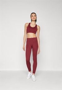 Sutien sport maroniu și colanți, realizați dintr-un material moale și elastic. Setul are un design ajustat și construcție fără cusături, asortat cu adidași albi.