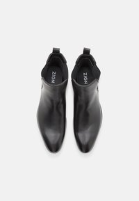 Paire de bottines Chelsea en cuir noir avec bouts pointus et panneaux latéraux élastiques, vue de dessus sur fond blanc.