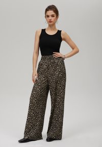 Svart ribbad linne i kombination med vida byxor med beige och svart leopardmönster. Outfiten kompletteras med svarta skor.