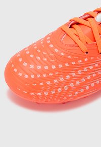 Zapato de fútbol naranja brillante con superficie texturizada. Patrón floral blanco y cordones rojos. Cuenta con tacos moldeados en la suela para tracción.