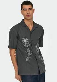 Grijs shirt met korte mouwen en zwarte knopen, voorzien van witte bloemenborduursels aan de linkerzijde en een relaxte pasvorm. Gemaakt van een katoenmix.