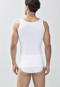 Biały bawełniany top na ramiączkach z klasycznym okrągłym dekoltem, dopasowany krój, bez widocznych logo, w połączeniu z białymi figami. Teksturowana tkanina, gładki wygląd.