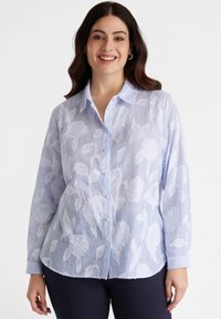 Camicia button-up azzurro chiaro con ricami floreali bianchi, texture a costine, maniche lunghe e colletto appuntito. Delicato motivo a righe.