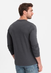 Grijze lange mouwen shirt van zachte stof, met een ronde hals en aansluitende mouwen, gecombineerd met blauwe denim jeans.