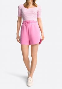 Růžové bavlněné kraťasy s elastickým pasem a šňůrkou, spojené s fitted bílým a růžovým pruhovaným tričkem. Neformální atletický vzhled.
